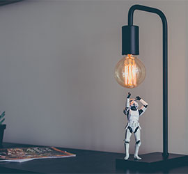 Desk lamp with an exposed bulb and a small astronaut figurine reaching up beside it