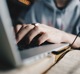 Close-up of hands typing on a laptop with a coffee cup on the desk