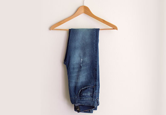 Dark blue jeans hanging on a wooden hanger