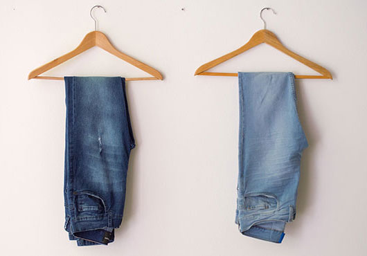 Two pairs of jeans hanging on wooden hangers