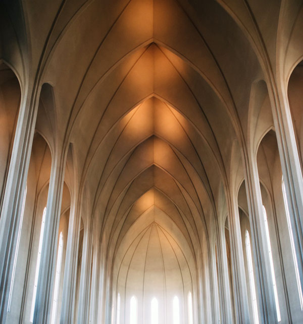 Interior of a cathedral with tall symmetrical arches and warm light streaming through narrow windows