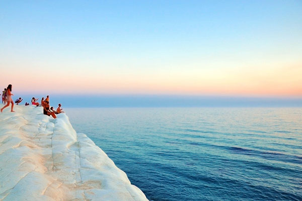 Group of people sitting on a white cliff overlooking the sea at sunset