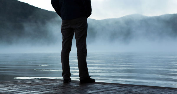 Person standing on a wooden dock looking out over a misty lake with mountains in the background