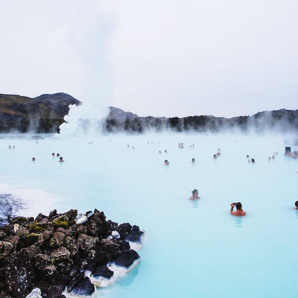 People bathing in a steaming geothermal lagoon with milky blue water and volcanic rocks