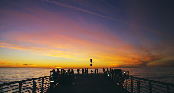 Silhouettes of people standing on a pier at sunset over the ocean