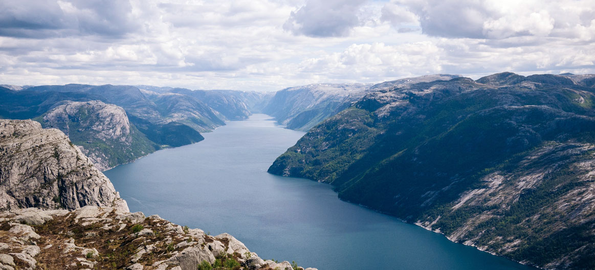 Aerial view of a long fjord-like river winding between steep rocky mountains under cloudy skies