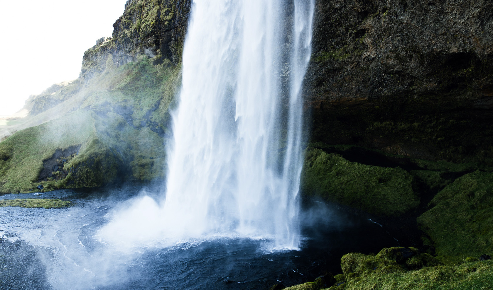 Tall waterfall plunging into a pool beneath a moss-covered cliff