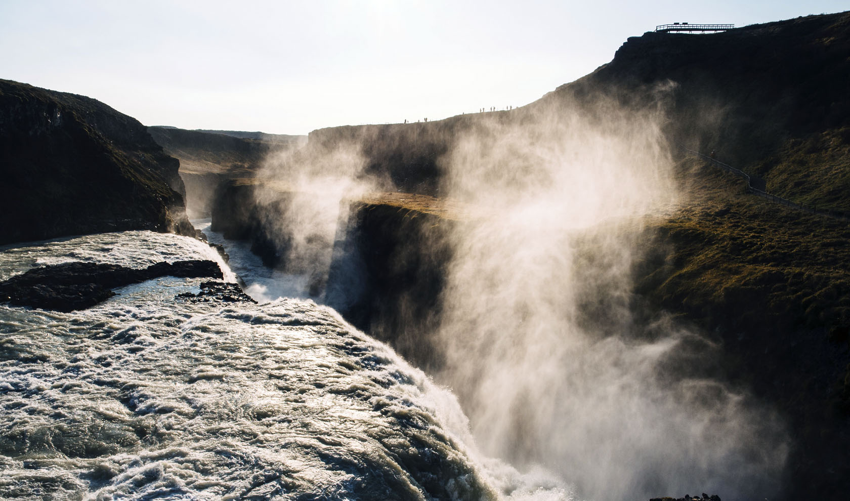 Wide river flowing through a rocky canyon with mist rising from the gorge