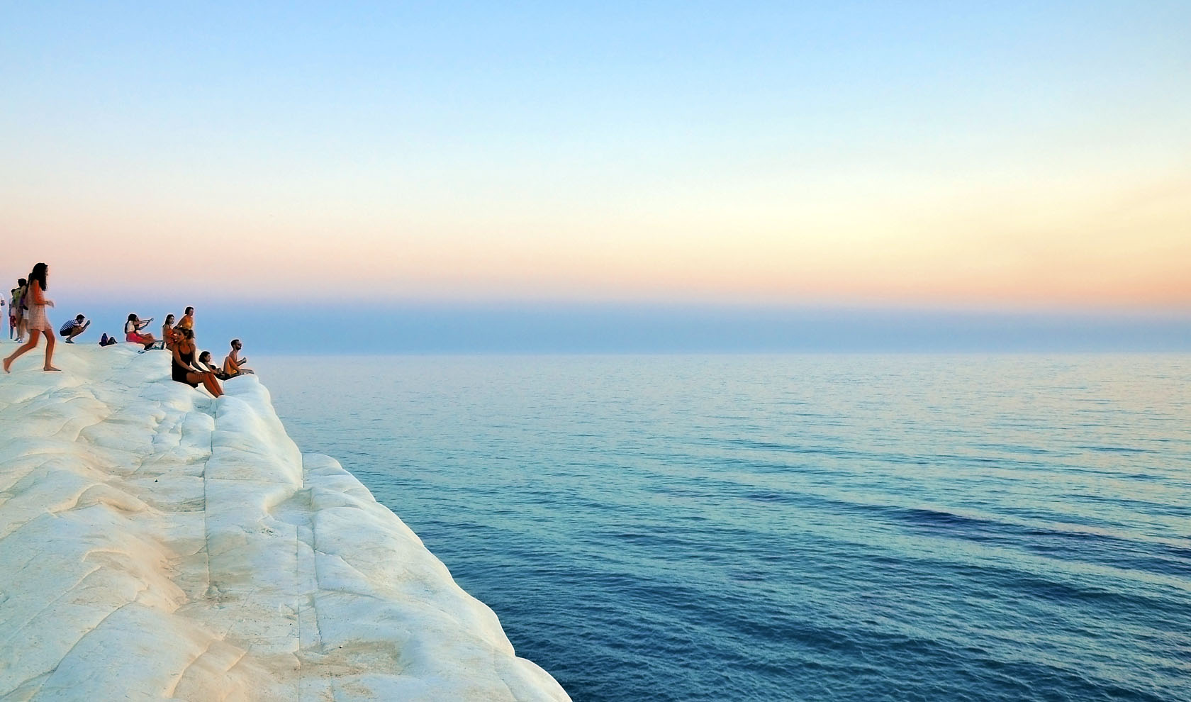People sitting on a white cliff edge overlooking the sea at sunset