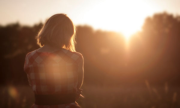 Person standing in a field watching the sun set over trees