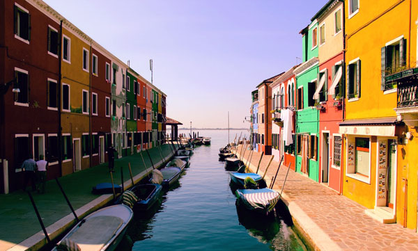 Colourful houses lining a canal with small boats moored along the water