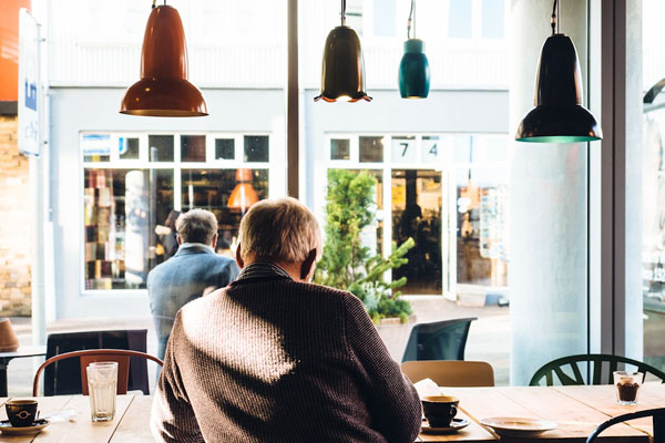 People sitting at a café table by a large window with hanging pendant lights