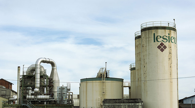 Industrial storage tanks and processing equipment at a factory facility under a cloudy sky during daytime