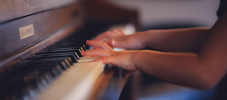Hands of a person playing a Baldwin piano with a shallow depth of field highlighting the keys and motion blur on the hands