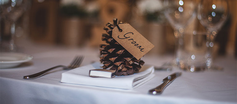 Pinecone place card labeled Groom set on a folded napkin at an elegantly arranged wedding reception table.