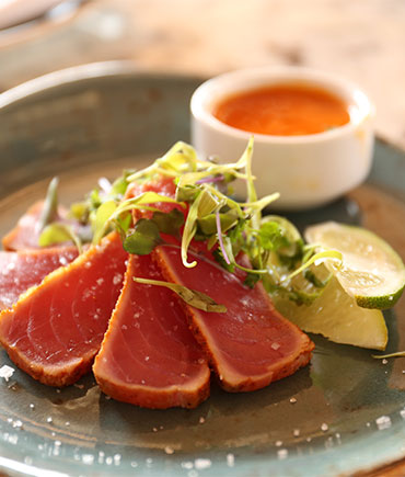 Seared tuna slices garnished with microgreens served with lime wedges and a small bowl of dipping sauce on a plate