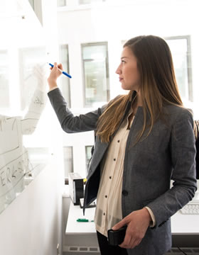 Young professional woman writing on a transparent board in a modern office environment during a workday.