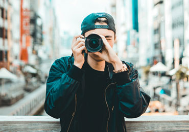 Young photographer wearing a backward cap taking a photo with a professional camera in an urban outdoor setting.
