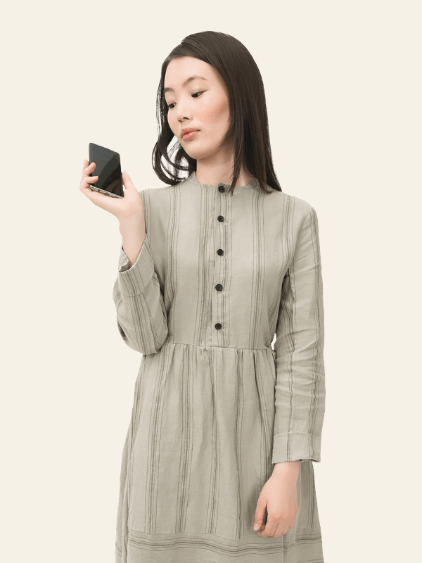 Young woman in a striped beige dress looking at a smartphone against a plain light background