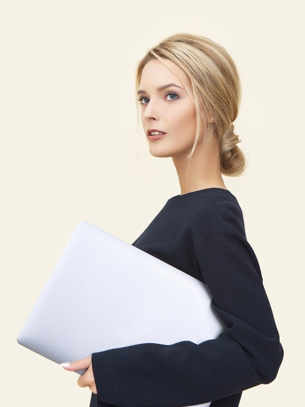 Young professional woman with blonde hair holding a closed laptop against a neutral beige background in a minimalistic style