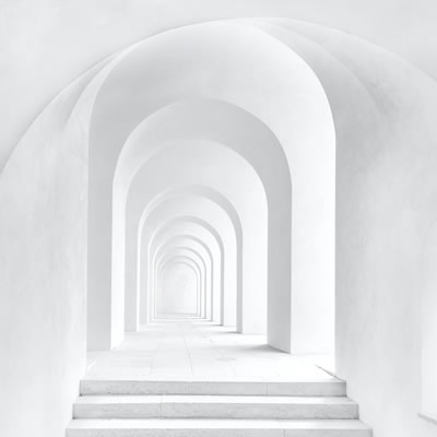 White arched corridor with repeating arches creating a bright, minimalist architectural walkway.