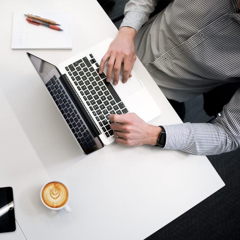 Overhead view of a person working on a laptop at a desk with a coffee cup and notepad, representing office or remote work.