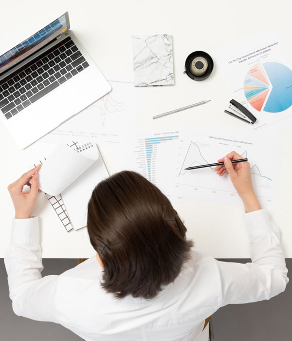 Overhead view of a person at a desk reviewing charts and graphs with a laptop and stationery, representing data analysis or business planning.