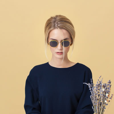 Studio portrait of a person wearing sunglasses against a light background, holding a small bouquet of dried flowers.