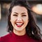 Smiling young woman with dark hair wearing a red top against a plain white background.