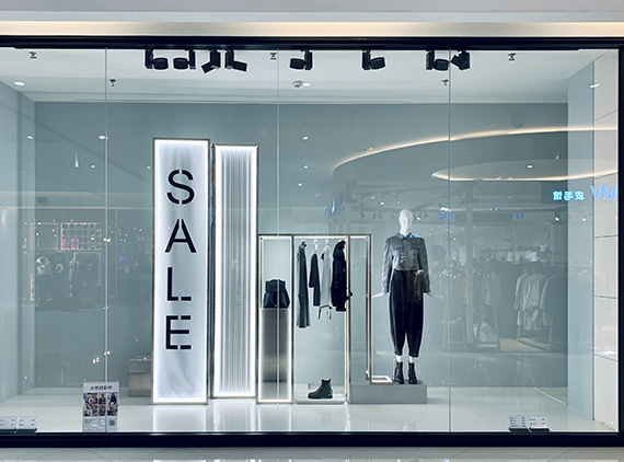 Modern shop window display with a large illuminated SALE sign and mannequins inside