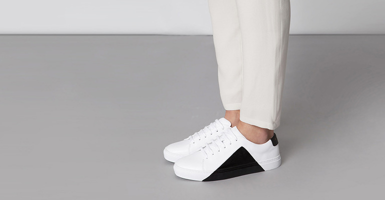 Person wearing white trainers and light trousers, standing on a studio floor