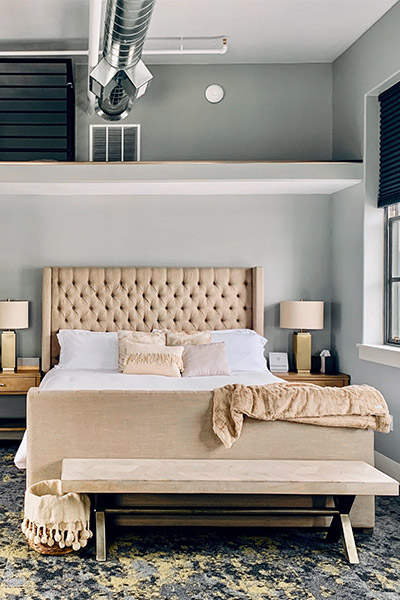 Stylish bedroom with a large upholstered bed, bedside tables with lamps, and modern industrial-style ceiling ducting.