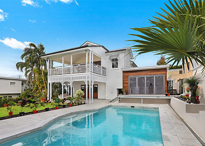 Exterior of a modern two-storey house with a swimming pool and landscaped garden in a sunny setting.