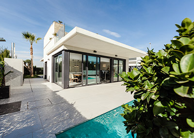 Exterior of a modern single-storey home with large glass doors opening onto a patio beside a swimming pool.
