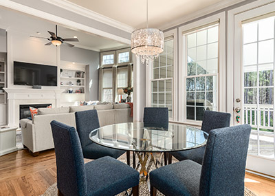 Bright, modern open-plan living and dining area with glass dining table, upholstered chairs, and large windows letting in natural light.