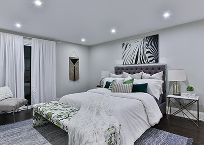 Contemporary bedroom with a large upholstered bed, patterned throw at the foot, bedside tables with lamps, and modern wall art.