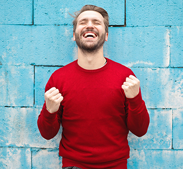 Man in red sweater expressing joy and excitement standing against a blue brick wall background.