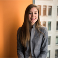 Young professional woman in gray blazer smiling confidently in an office setting with natural light background