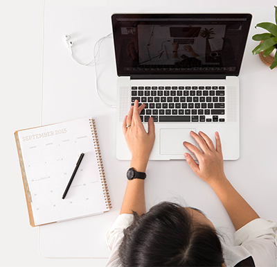 Person working on a laptop with a September 2015 calendar and a pen on the white desk surface around them.