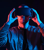 A person wearing a virtual reality headset, illuminated by blue and purple lighting, suggests immersion in a digital world.