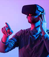 Wearing a virtual reality headset, a man engages with a digital environment while illuminated by vibrant purple and blue lighting.