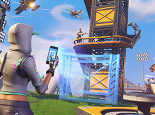 Character in a hoodie using a device to build a structure while airborne opponents approach in a video game battle scene.