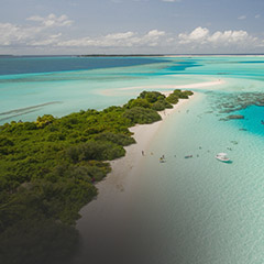 Aerial view of a tropical island with white sandy beaches, turquoise waters, lush greenery, and boats anchored near the shore.