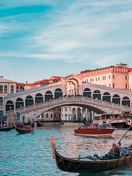 Historic Rialto Bridge over the Grand Canal in Venice with gondolas and boats on a sunny day.