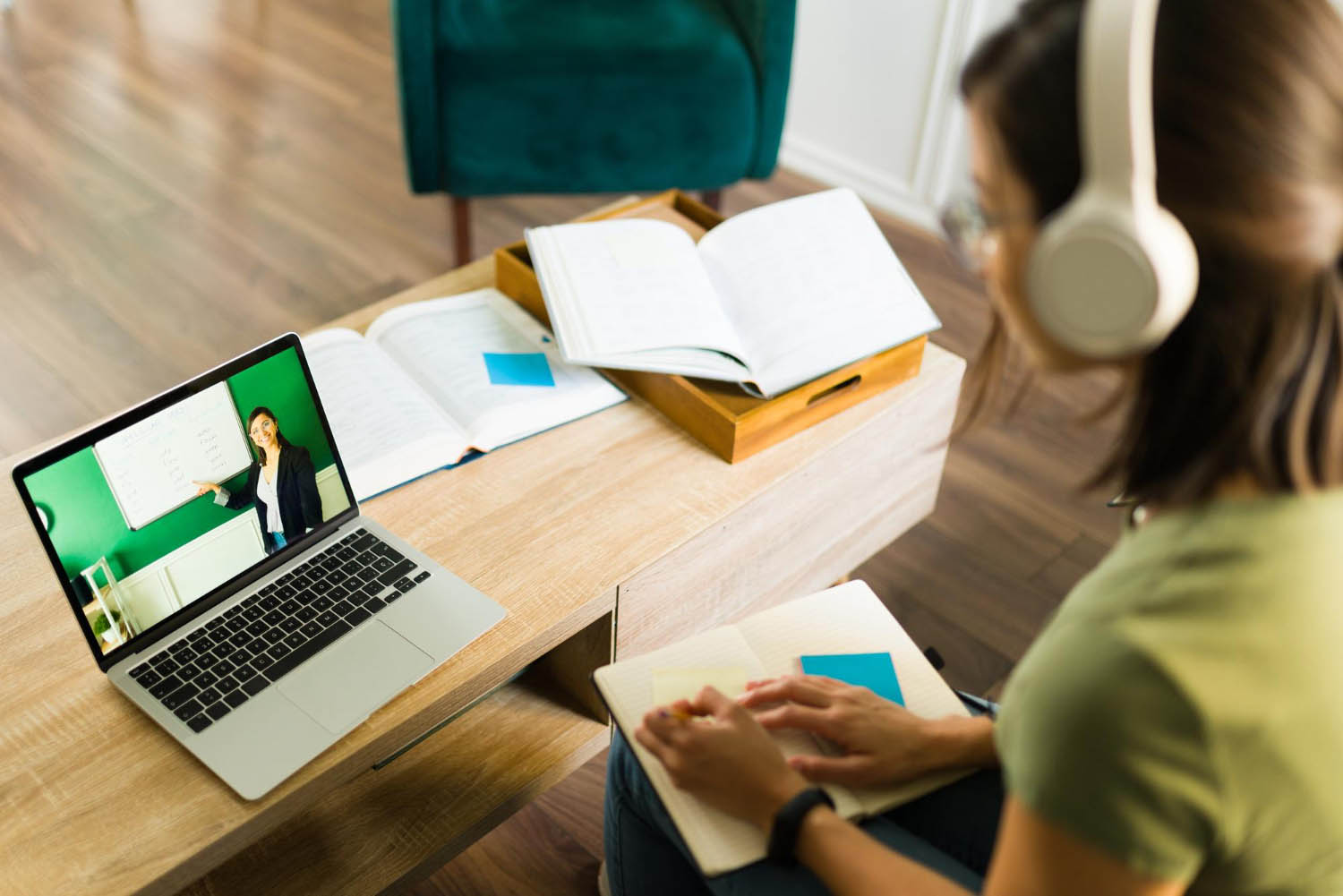 Student wearing headphones taking notes while watching an online lesson on a laptop, representing remote learning or online education.